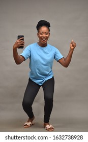 pretty young black woman dressed casual holding her mobile phone, celebrating