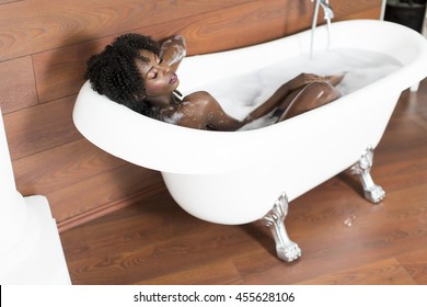 Pretty young black woman having a foam bath in the room