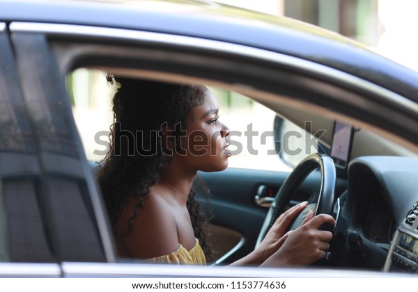 Pretty young black woman\
having problems while driving car and looking frustrated pressing\
car horn