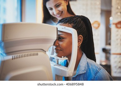 Pretty young black woman presses her forehead to optical machine to take eye exam