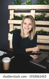 Pretty Young Blond Woman Is Sitting In A Modern, Sustainable Office With Lots Of Green Ecological Plants And Is Working On Her Tablet
