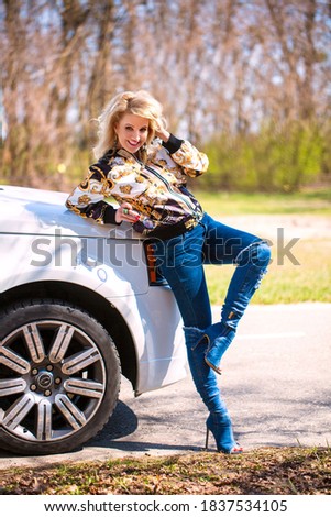 Pretty young blonde girl in a casual clothes and jeans staying near the modern luxury off-road car