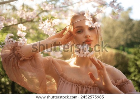 Pretty young blonde girl with  in vintage pink dress standing in spring park near pink blossom flowers. Tenderness romantic  model posing with emotions.