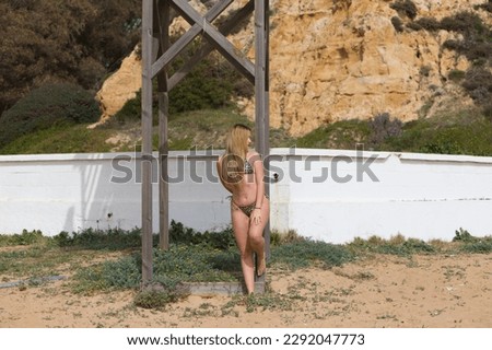 Pretty young blonde woman leaning on the wooden poster of the lifeguard tower on the beach. The woman is wearing a leopard bikini and enjoying her summer holiday.