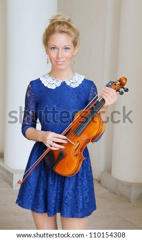 Pretty young blonde woman with violin near house