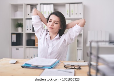 Pretty Young Brunette Businesswoman Or Manager With Her Hands Behind Head Sitting In Armchair And Relaxing In Office Environment