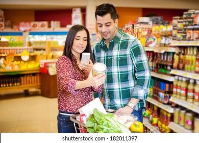 Pretty Young Brunette And Her Partner Taking A Picture Of A Product With Her Cell Phone At A Grocery Store