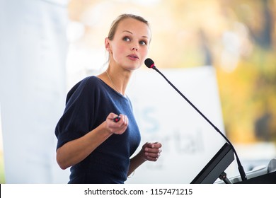 Hübsche junge Geschäftsfrau, die eine Präsentation in einem Konferenz-/Tagungsraum (flacher DOF) hält; Farbtonbild)