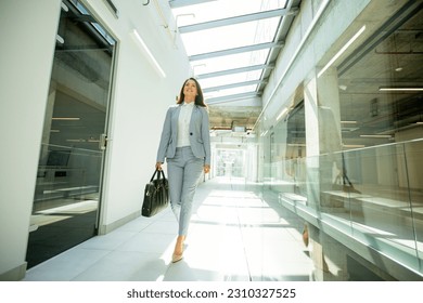 Pretty young business woman walking with briefcase in office hallway - Powered by Shutterstock