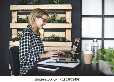 pretty, young businesswoman with a black and white checked shirt and black glasses sits in a sustainable, ecological office and works on the laptop