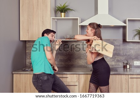 Pretty young caucasian couple about 22 years old had some problems in their relationship and have a fight in the kitchen with help of cutting board.