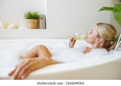 Pretty Young Caucasian Female Relaxing In Bath With Bubbles And Sipping White Wine.