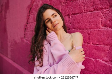 Pretty Young Caucasian Girl Looking Into Distance Stands Alone Near Pink Building Wall. Brown Hair Woman Wears Pink Cardigan. Concept Tenderness.