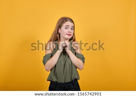 Pretty young caucasian lady keeping fists on chest with over orange background. Looks happy, funny wearing haki shirt