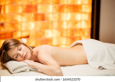 pretty young caucasian woman 20-25 years old lying on bed with naked back and closed eyes at spa, waiting for massage by professional masseur. yellow wall in the background. keep calm and relax