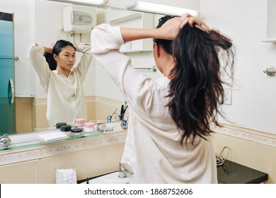 Pretty Young Chienese Woman In White Shirt Making High Ponytail In Front Of Mirror In Bathroom