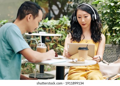 Pretty young Chinese woman with tablet computer making videocall when her boyfriend taking notes in textbook - Shutterstock ID 1911899134