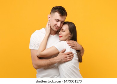 Pretty Young Couple Two Friends Guy Girl In White Empty Blank Design T-shirts Posing Isolated On Yellow Orange Background. People Lifestyle Concept. Mock Up Copy Space. Hugging, Keeping Eyes Closed