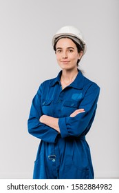Pretty young cross-armed female engineer in blue workwear and safety helmet standing in isolation - Shutterstock ID 1582884982