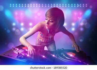 Pretty young disc jockey mixing music on turntables on stage with lights and stroboscopes