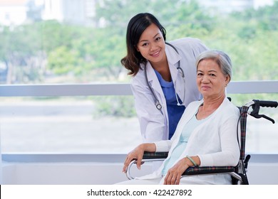 Pretty young doctor caring about elderly woman in wheelchair