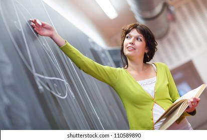 Pretty young elementary school/college teacher writing on the chalkboard/blackboard during a math class (color toned image; shallow DOF) - Powered by Shutterstock