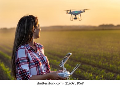 Pretty young farmer woman driving drone with remote control in front of tractor in soybean field in spring at evening - Shutterstock ID 2160931069