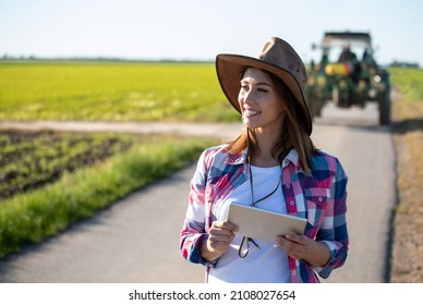 Pretty Young Farmer Woman Working On Tablet In Front Of Tractor