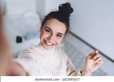 Hübsches junges Weibchen mit großem Lächeln, das nach der Arbeit mit dem Laptop im Schlafzimmer steht und sich auf unscharfem Hintergrund gut amüsiert