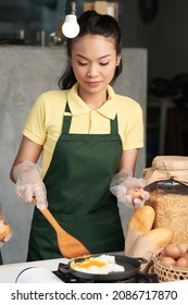 Pretty Young Female Cook In Green Apron Frying Eggs When Cooking Dish For Customer