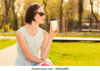 Pretty young female drinking coffee outside in the park and resting in the nature