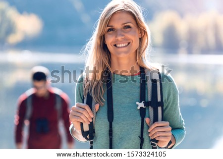 Pretty young female hiker smiling while looking at camera in front of lake.