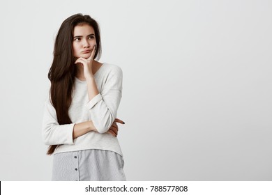 Pretty Young Female With Long Dark Hair Looking Away Holding Hand Under Chin, Building Plans, Thinking About Something. Pensive Brunette Beautiful Girl With Thoughtful And Pensive Face Expression