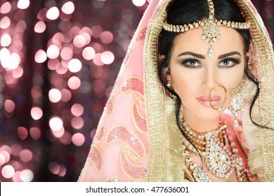 A pretty young female model wearing traditional indian pakistani bridal outfit with heavy jewelry and makeup
