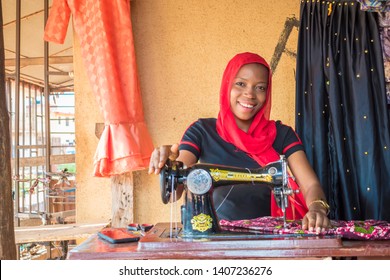 pretty young female tailor smiling while sewing a dress