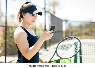 Pretty young female tennis player on court using smart phone during a break in training - Powered by Shutterstock