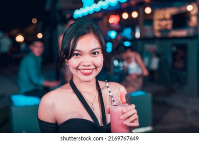A Pretty Young FIlipino Woman Enjoying A Watermelon Shake At An Outdoor Bar. A Young Person Drinking Nonalcoholic Drinks. Nightlife Scene.
