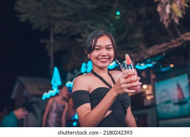 A Pretty Young FIlipino Woman Enjoying A Watermelon Shake At An Outdoor Bar. A Young Person Drinking Non-alcoholic Drinks. Nightlife Scene.