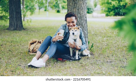 Pretty young girl blogger is taking selfie with adorable purebred dog outdoors in city park cuddling and fondling beautiful animal. Modern technology, loving animals and nature concept. - Powered by Shutterstock