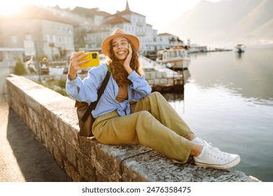 Pretty young girl enjoying the sunny weather on the viewpoint.  Woman making selfie on smartphone for her stories in social network. Travelling as lifestyle. - Powered by Shutterstock