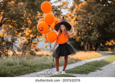 Hübsches junges Mädchen mit orangefarbenen Halbwertsballons und Hemd, schwarzem Rock, Hut und Hexensocken, die auf der Straße stehen. Halloween-Konzept. Kopiert Platz.