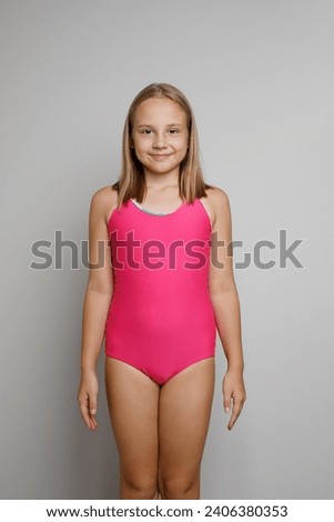 Pretty young girl in pink swimsuit posing on light gray studio wall background. Travel, sport, swimming activities and vacations concept