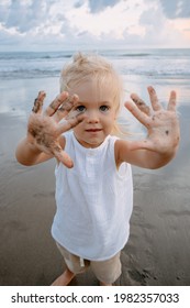 Pretty Young Girl Showing Messy Hands In Dark Sand. Beach And Ocean Background, Summer Vacation 