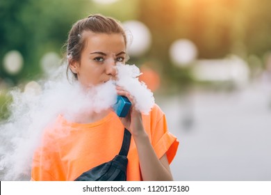 Pretty young hipster woman vape ecig, vaping device at the sunset. Toned image.