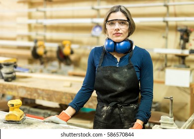 Pretty young Hispanic female carpenter wearing protective equipment in a woodshop - Powered by Shutterstock