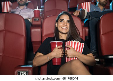 Pretty Young Hispanic Woman Hugging Her Snack Combo Of Soda And Popcorn At The Movie Theater And Smiling