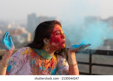 Pretty Young indian smart girl with face coloured with gulal for festival of colours Holi blowing holi color powder, a popular hindu festival celebrated across india - Shutterstock ID 2130544247