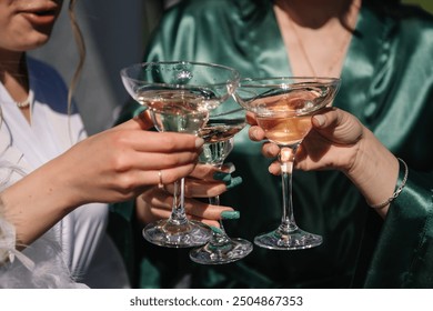 Pretty young ladies friends wear silk robes hold glasses with champagne in hotel. Bride and bridesmaid celebrate bachelorette spa party. Cheers. Closeup three female hands holding cocktails and drink. - Powered by Shutterstock