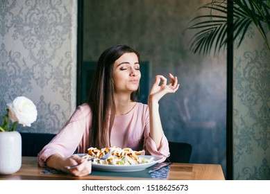 Pretty young lady sitting in a beautiful restaurant, enjoying lunch or dinner and making delicious hand gesture to express how good the food is. 