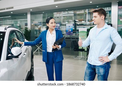 Pretty young manager showing automobile to smiling young car dealership client - Shutterstock ID 1868732740